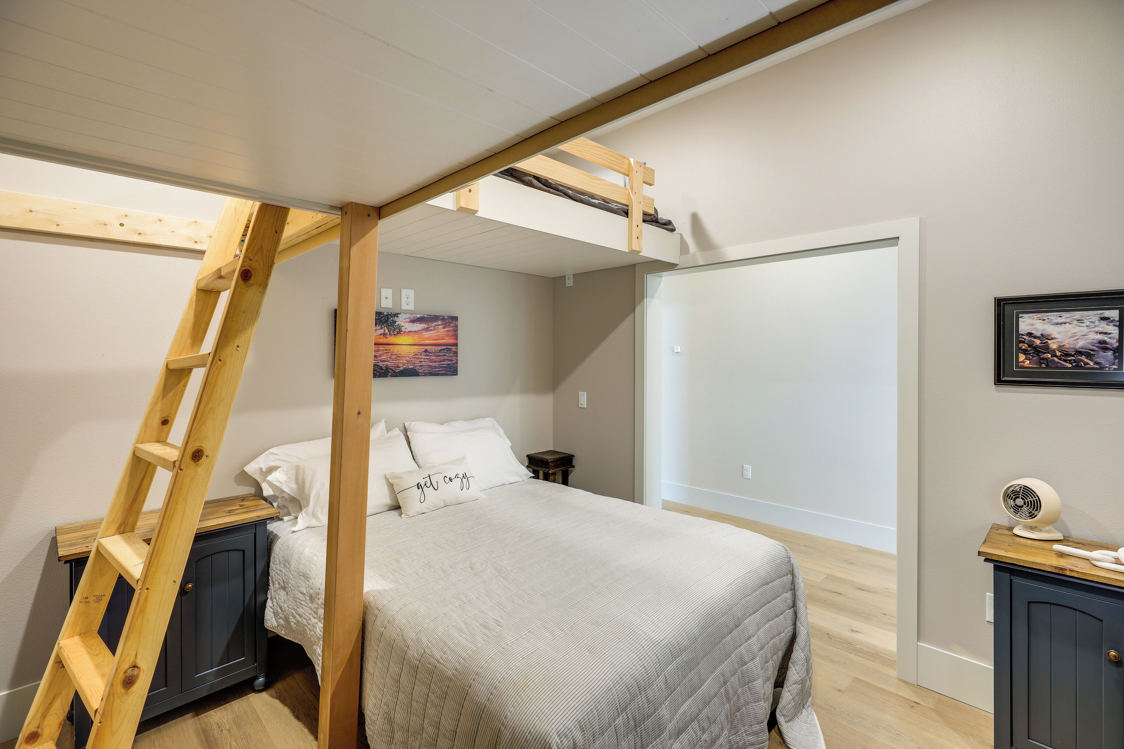Ein Schlafzimmer mit Etagenbett, einer Sprosse, einem Nachttisch, einem Beistelltisch, einem Bett mit Steppdecke und einem Wandventilator.