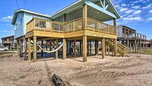 Una casa de playa de madera de dos pisos con un balcón y un porche cubierto.