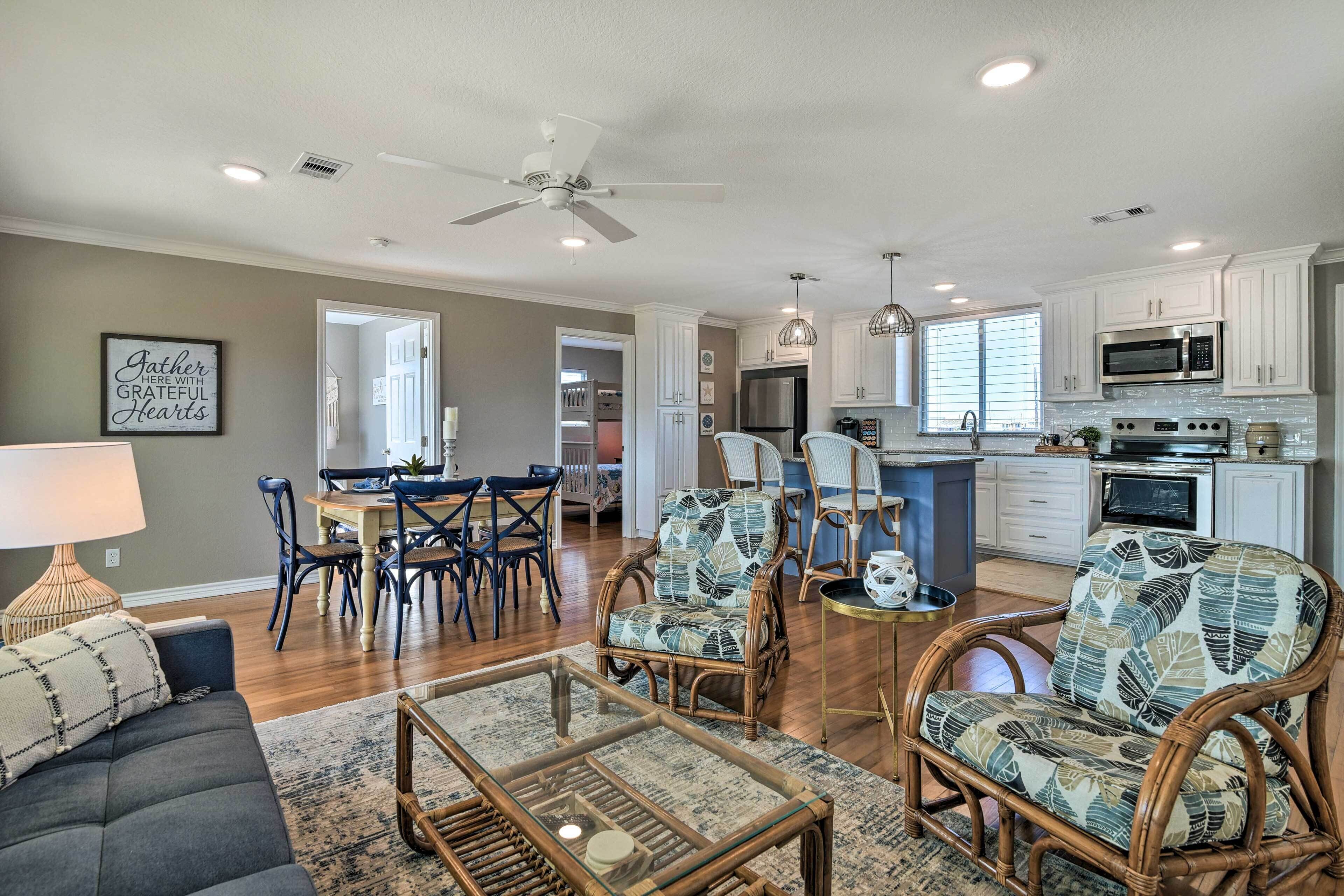 A spacious living room with a dark sofa, wicker chairs, a glass coffee table, and a dining area with a wooden table and chairs.