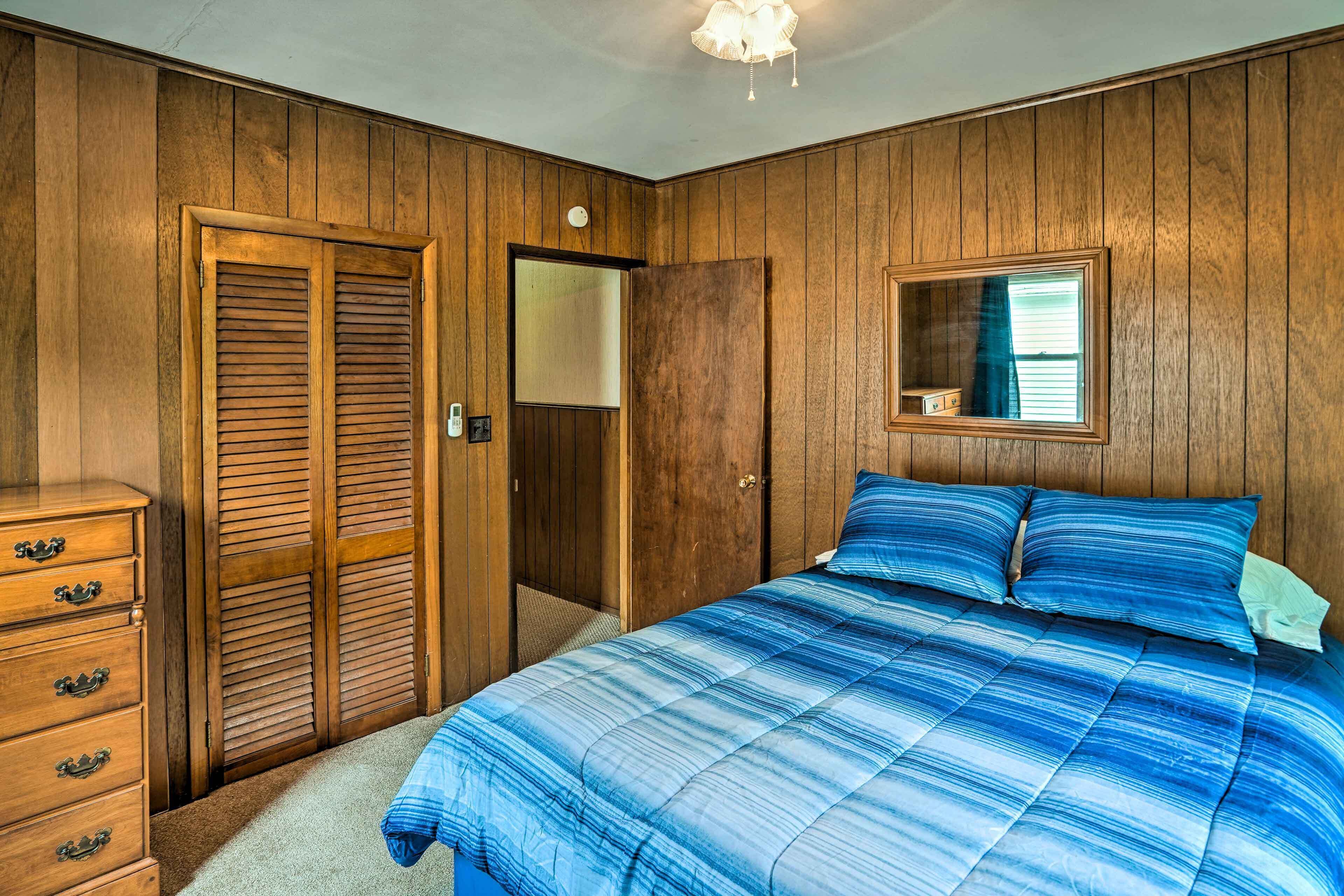 A bedroom with wooden paneling, a bed with blue bedding, a dresser, and a mirror on the wall.