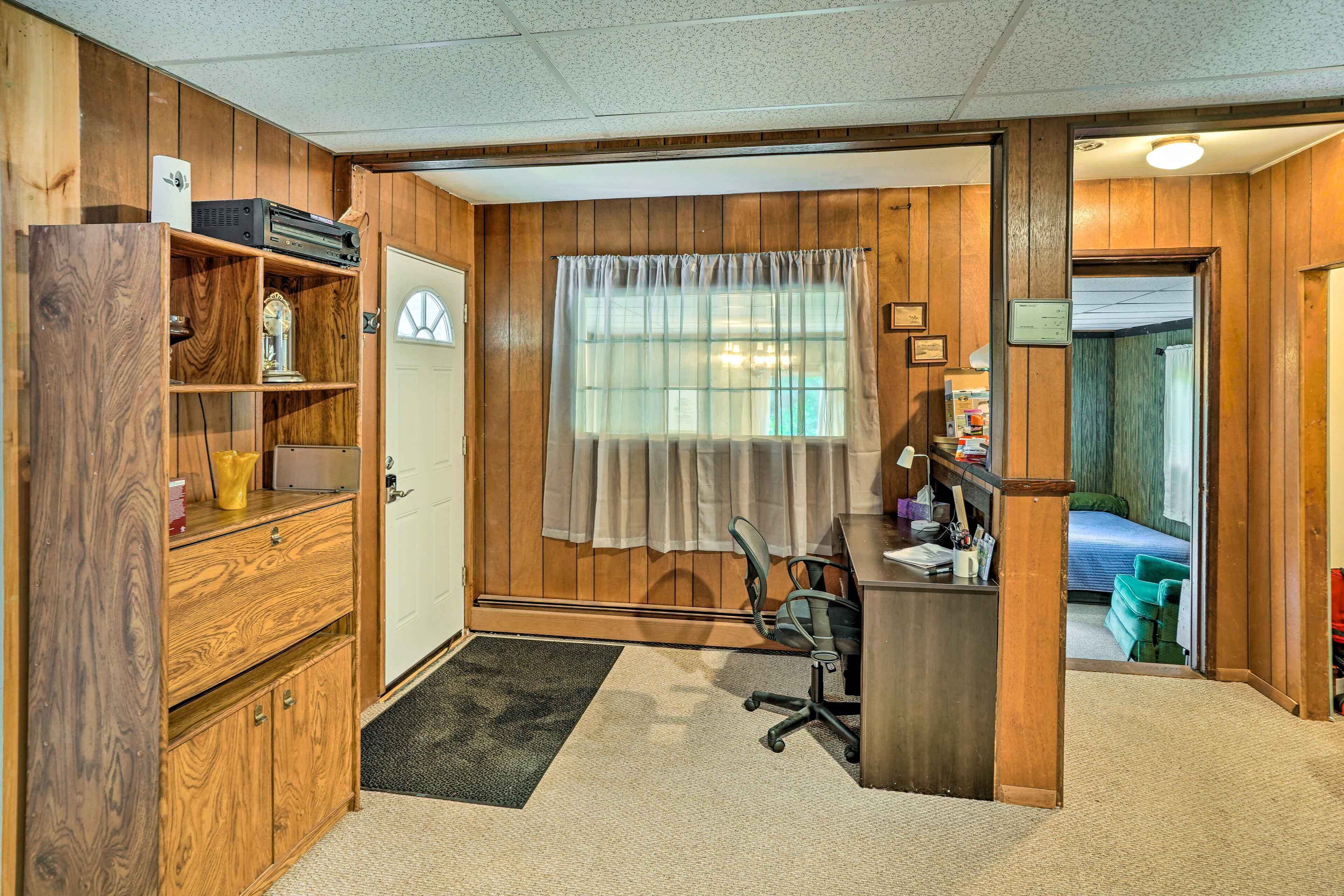 A compact room with a wooden desk, a chair, a small bookshelf, and a door leading to another room.
