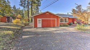 A red single-story house with a garage, surrounded by trees and a gravel driveway. - Willow Creek Hideaway w/ Deck, 1 Mi to River! (Willow Creek)