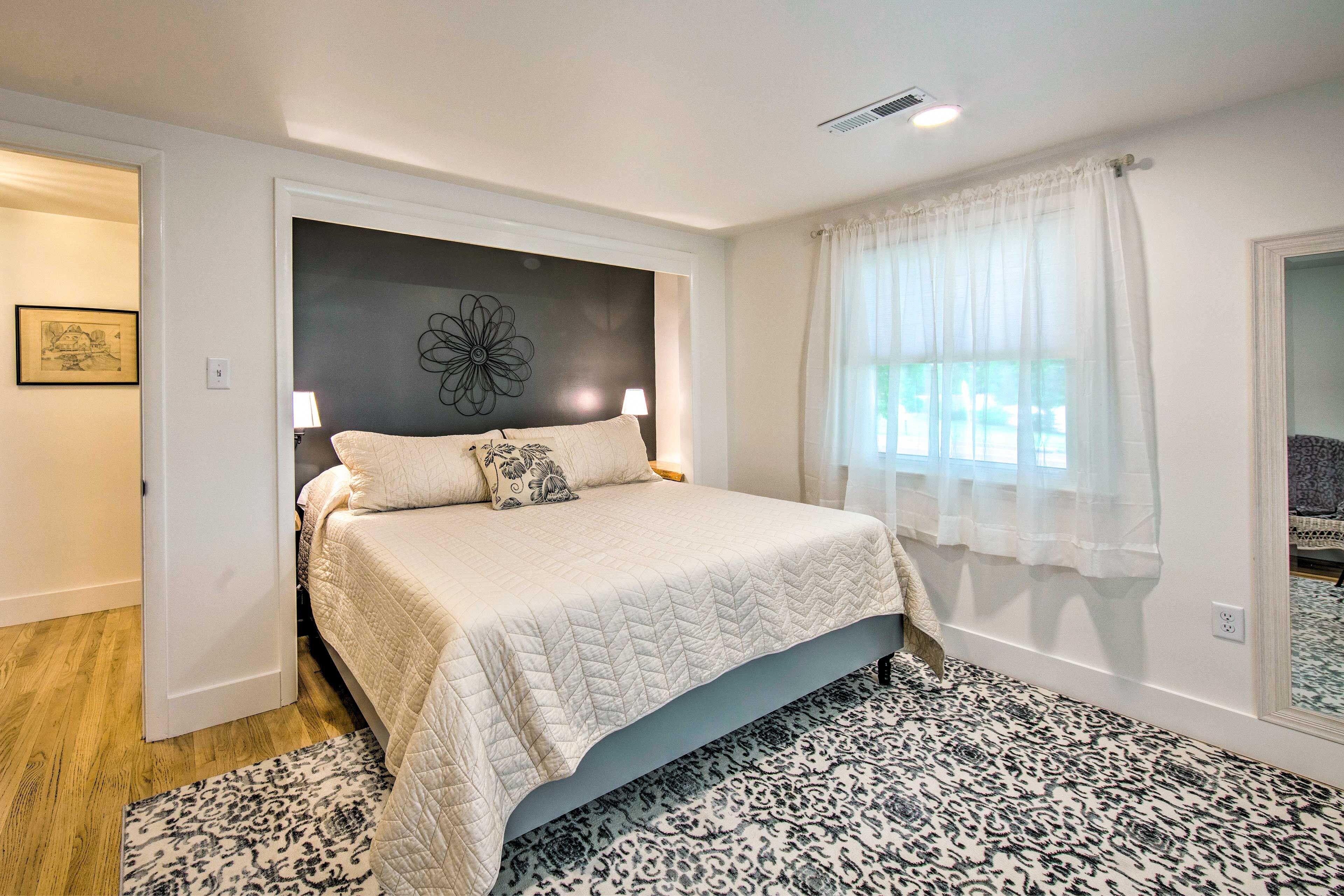 A bedroom with a bed, a patterned rug, a wall art piece, and a window with curtains.