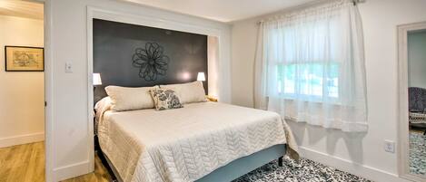 A bedroom with a bed, a patterned rug, a wall art piece, and a window with curtains.