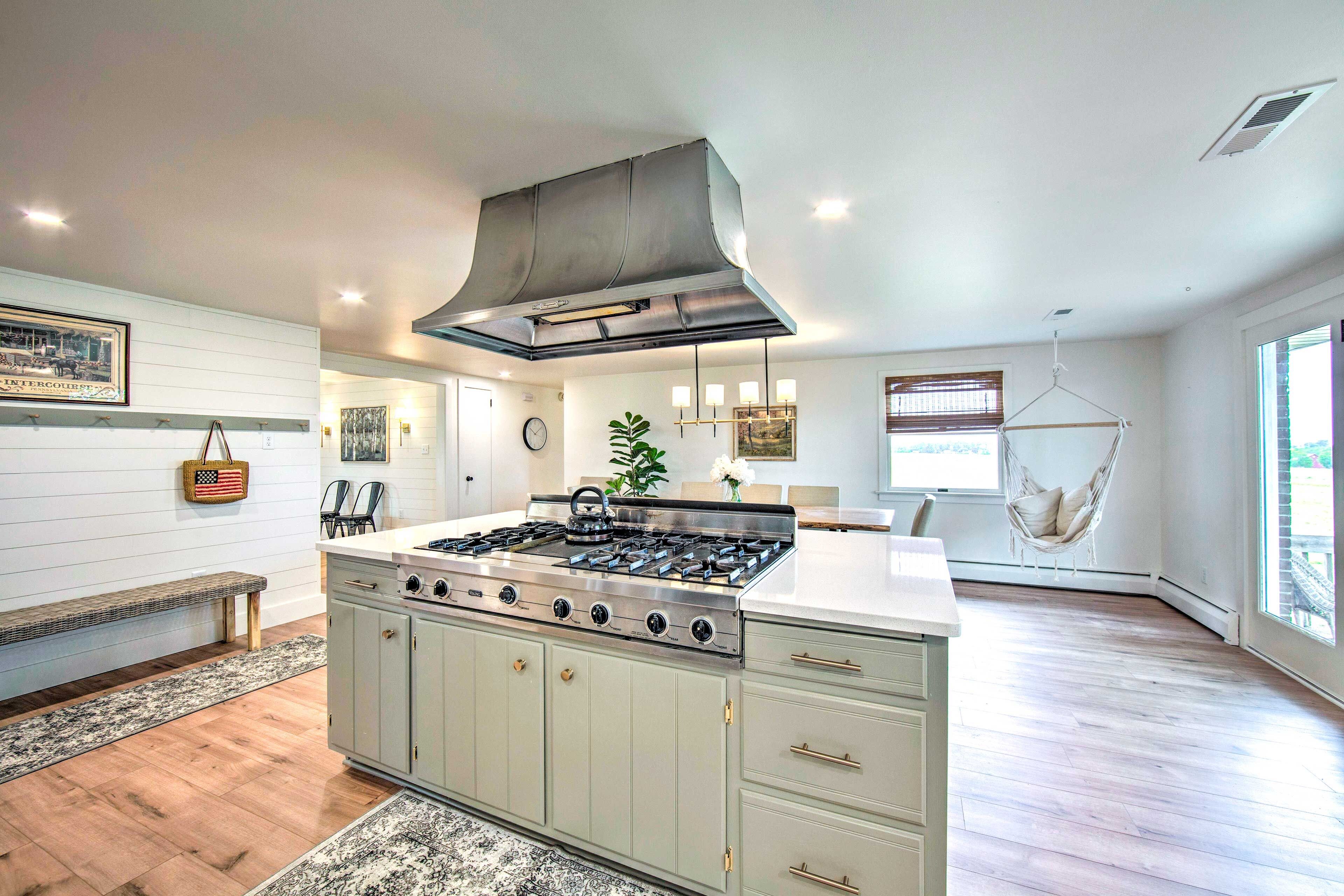A kitchen with a central island, a stove, and a hanging light fixture.