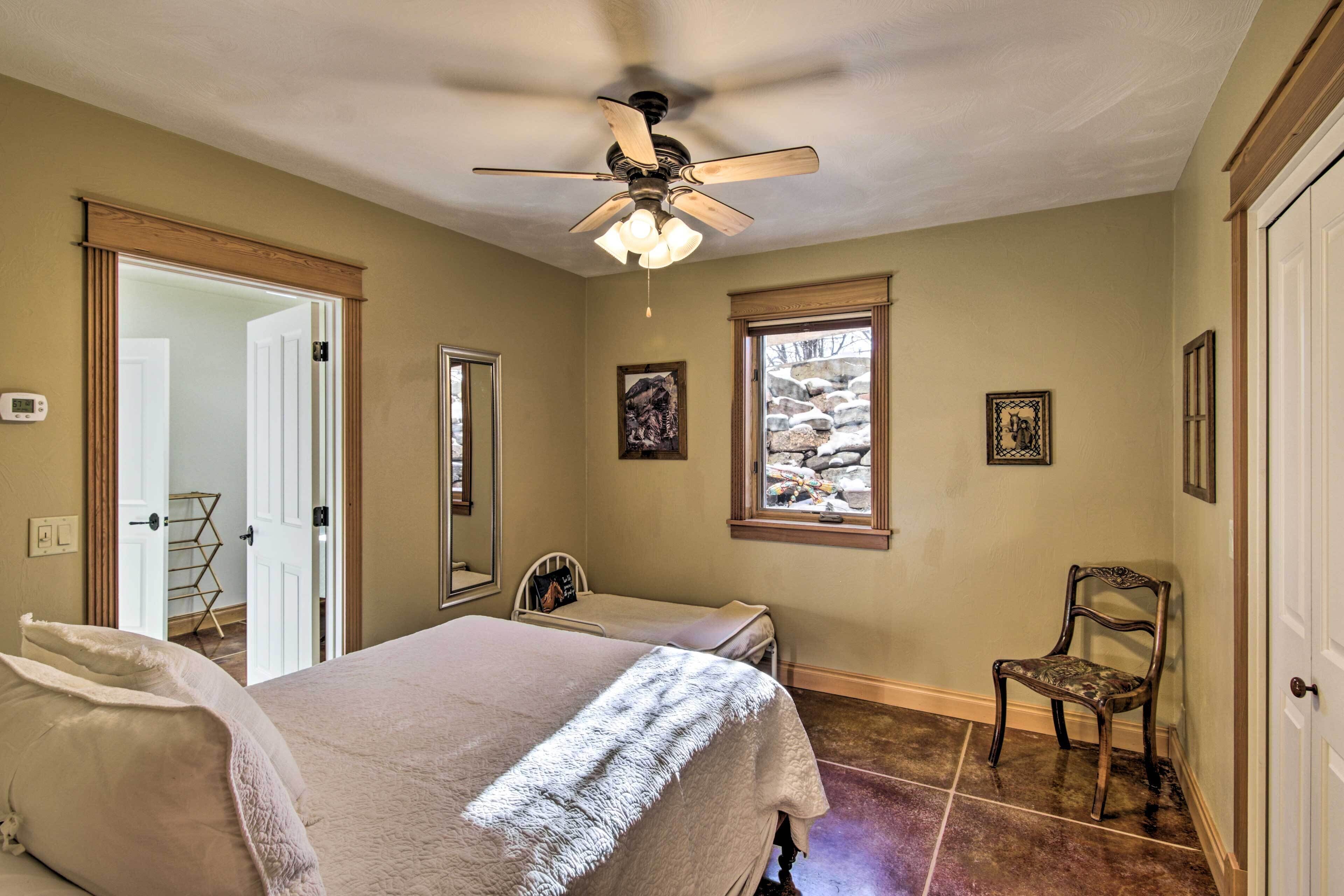 A bedroom with a bed, a chair, a ceiling fan, and a window with a view of rocks.