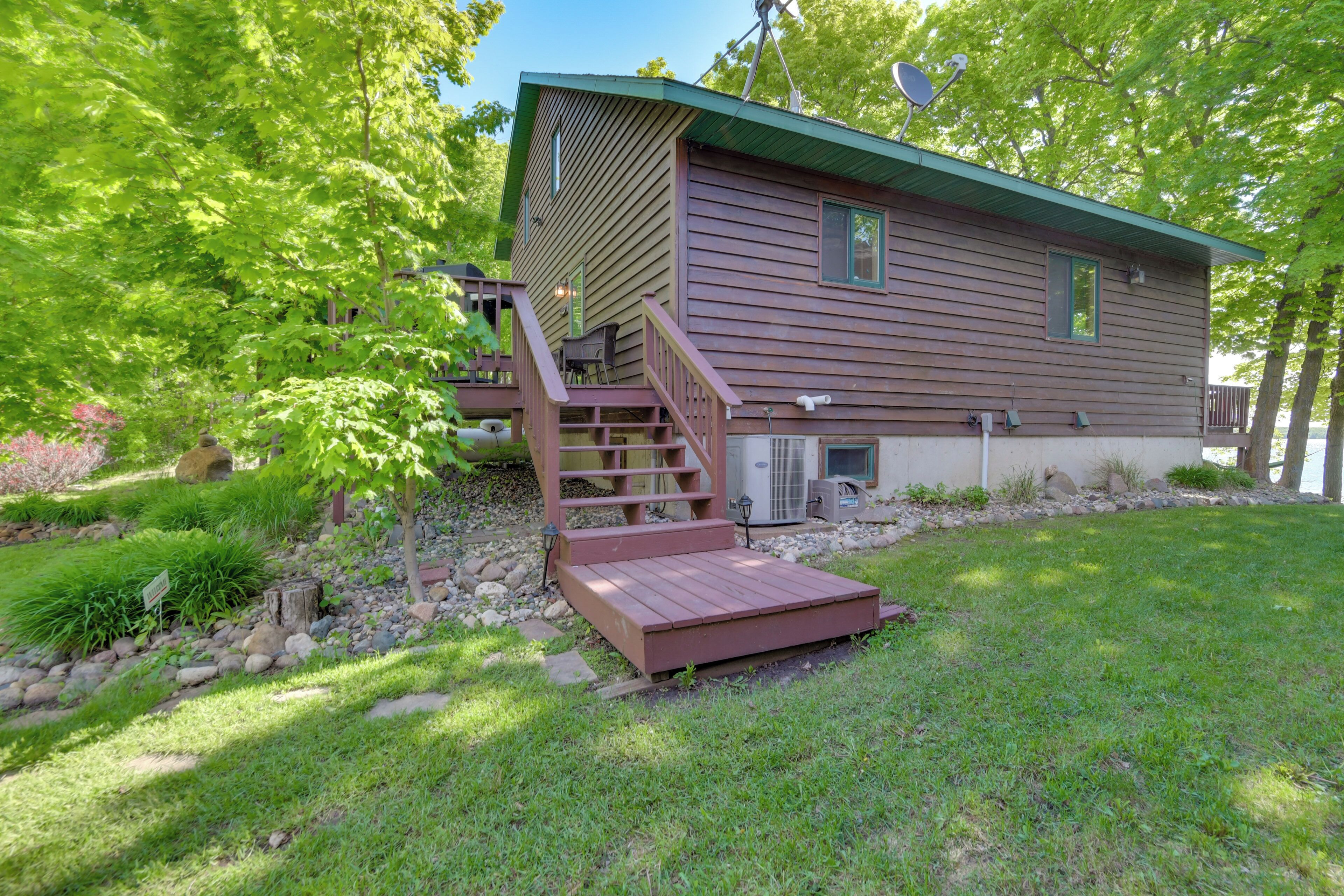 A two-story wooden cabin with a green roof, a front porch, and a small deck.