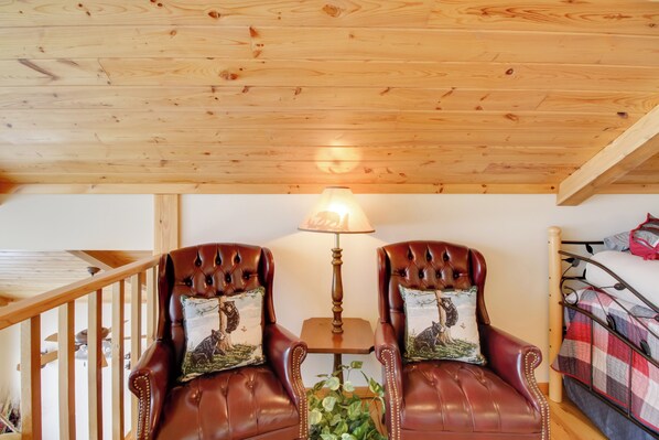 Una habitación con dos sillones de cuero, una mesita con lámpara, una cama con manta escocesa y techo de madera.