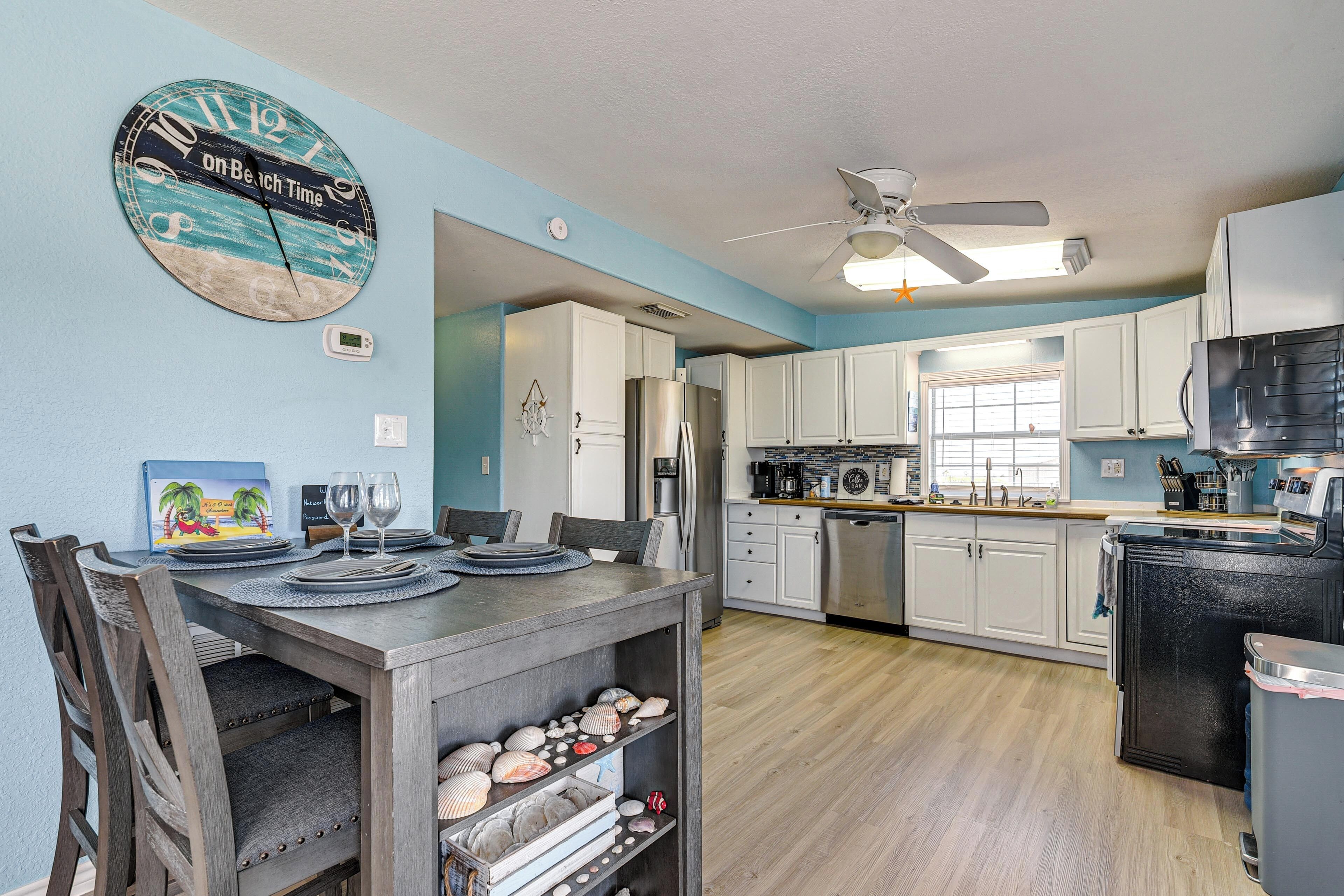 A kitchen with white cabinets, a refrigerator, a dining table with chairs, and a clock on the wall.
