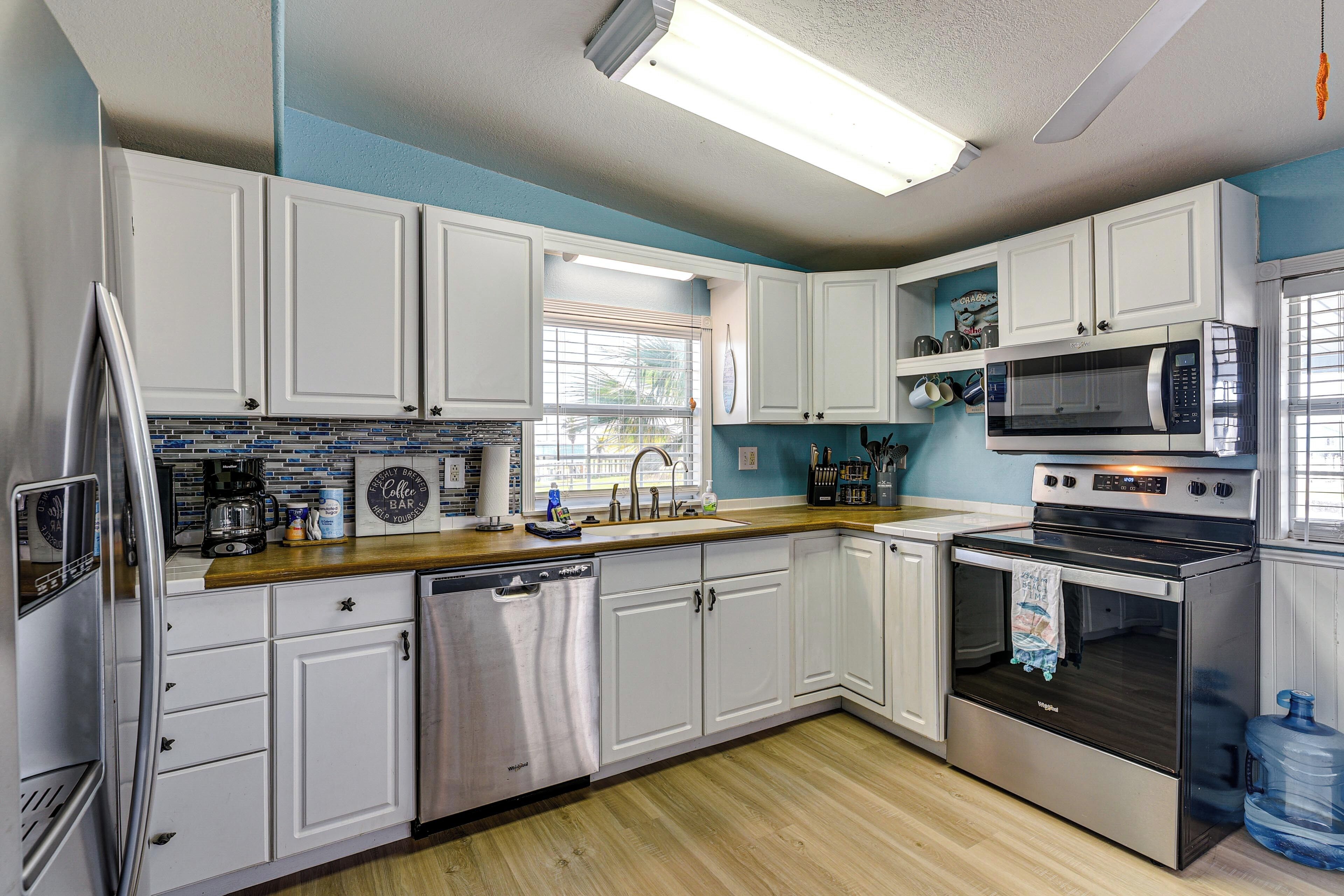 A modern kitchen with white cabinets, stainless steel appliances, and a blue accent wall.
