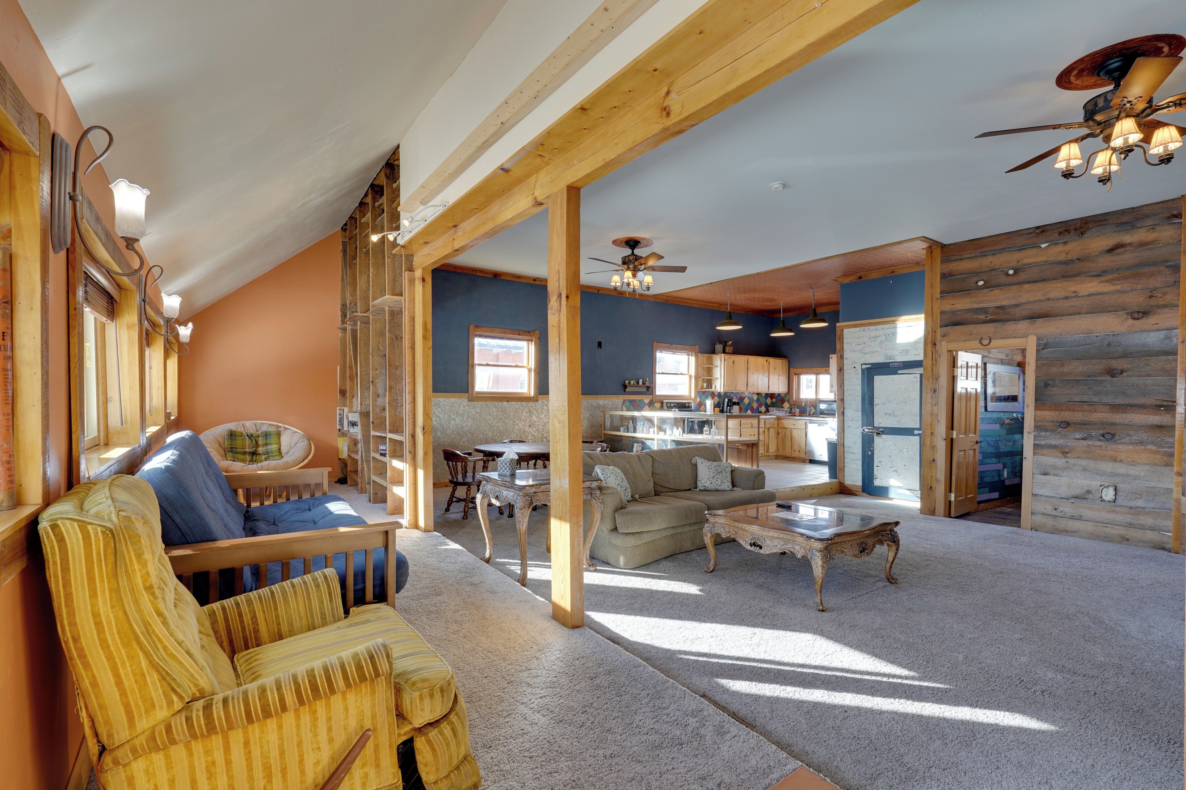 A spacious living room with a sofa, armchair, and coffee table. There is a dining area with a table and chairs, and a kitchen area with cabinets and a countertop.