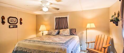 A bedroom with a bed, two bedside lamps, a ceiling fan, a wooden chair, and wall-mounted decorations.