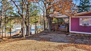 A rustic cabin with a wooden deck and a covered area, surrounded by trees and a view of a lake. - Waterfront House w/ Boat Slip on Lake Eufaula! (Canadian)