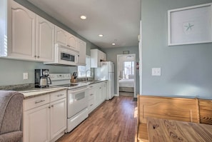 A compact kitchen with white cabinets, a microwave, a stove, and a refrigerator. There is a wooden bench and a small table in the dining area. - York Beachfront Condo - Steps to Long Sands! (York Beach)