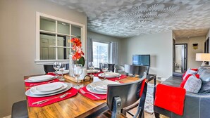 A dining area with a wooden table set for four, a vase with flowers, and a modern ceiling design.