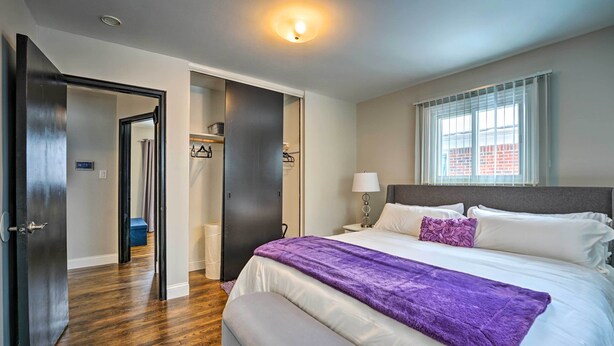 A hotel room with a large bed, a nightstand, a lamp, and a window with blinds.