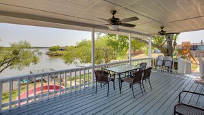 Eine überdachte Terrasse im Freien mit Tisch und Stühlen, mit Blick auf einen See und einen Spielplatz.