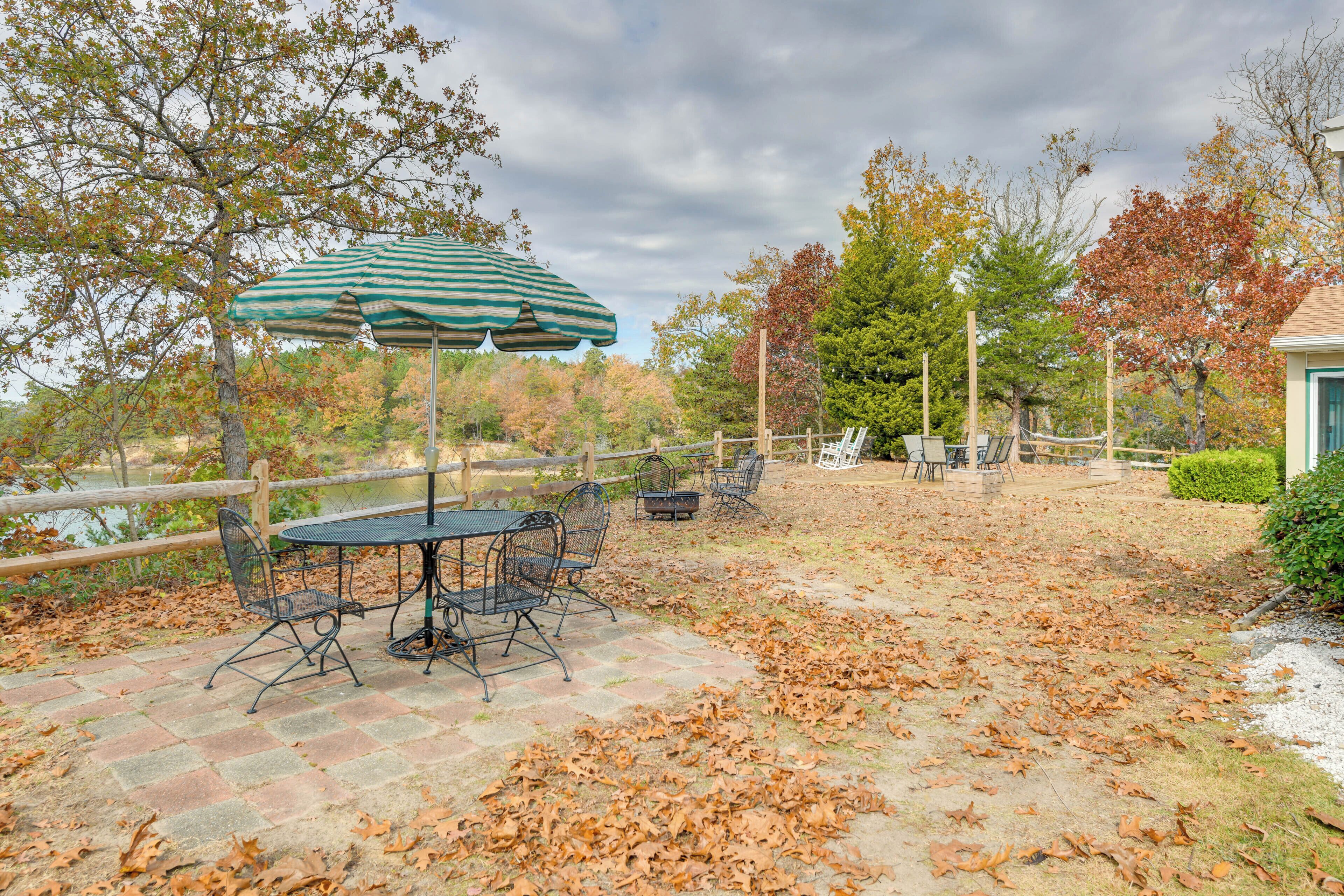 An outdoor patio with a table and chairs, a striped umbrella, and a view of a lake.