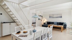 Un appartement moderne avec un escalier blanc, un coin repas comprenant une table et des chaises, un canapé et un tableau accroché au mur.