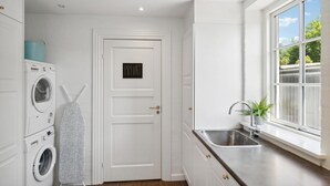 Une cuisine compacte équipée d’un lave-linge intégré, d’un évier et d’une fenêtre donnant sur la verdure.