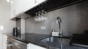 Eine moderne Küche mit Dunstabzugshaube aus Edelstahl, Backofen, doppelter Spüle und Weinkühlschrank mit Gläsern.