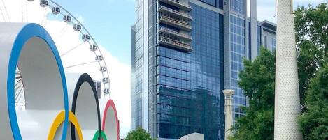 A modern building with a glass facade, a large Olympic rings sculpture, and a column with the number 100.