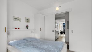 Ein Schlafzimmer mit Bett, Schreibtisch und Stuhl. Ein Fenster und eine Tür zu einem anderen Raum.