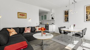 Ein modernes Wohnzimmer mit einem grauen Sofa, einem runden Couchtisch und einem Essbereich mit weißem Tisch und Stühlen.