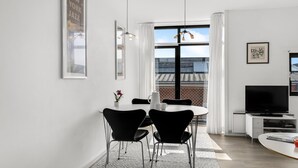 Ein modernes Wohnzimmer mit Essbereich, Fernseher und Blick auf die Stadtlandschaft.