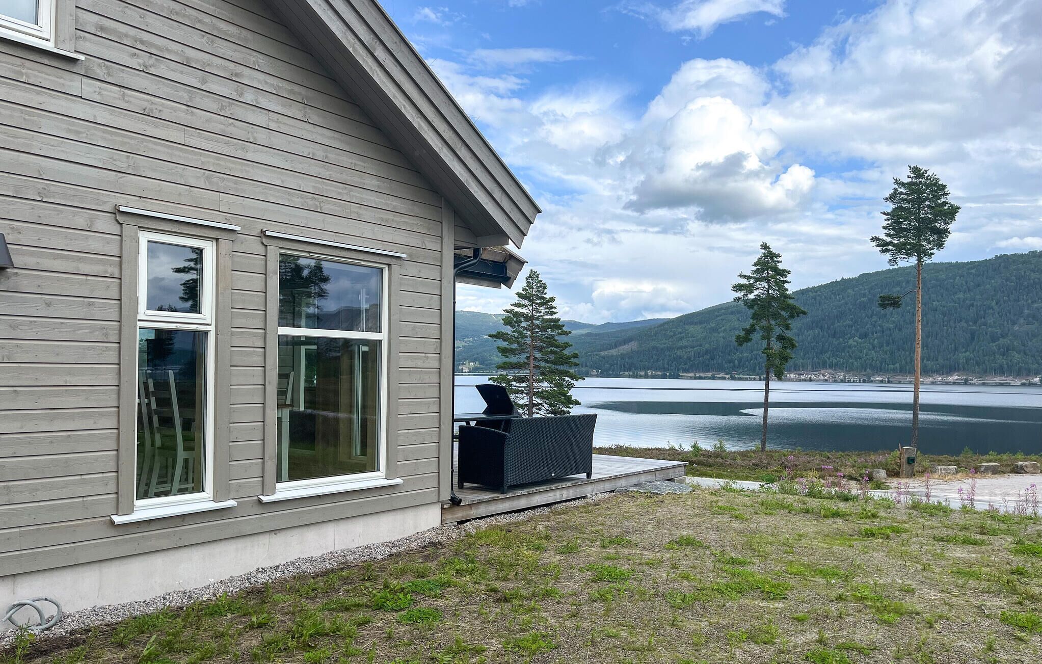 Une maison dotée d’une grande fenêtre donnant sur un lac et des montagnes.