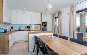 Enjoy cooking in this well-lit kitchen with a sink and compact oven, adjacent to a dining area with a wooden table and outdoor views.