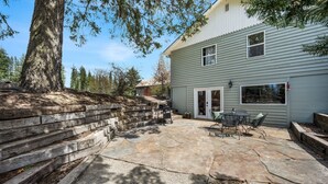 A patio area with stone flooring, a wooden retaining wall, and a house with a gray exterior.