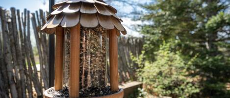 A bird feeder with a wooden structure and a circular base, surrounded by a wooden fence and greenery.