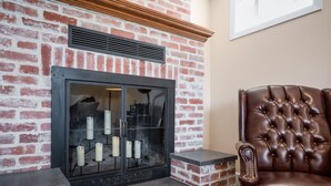 A fireplace with a brick wall, a leather chair, and a framed picture on the wall.
