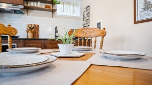 A dining table set with plates and a potted plant, wooden chairs, and a kitchen in the background.