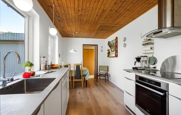 A modern kitchen with wooden ceiling, stainless steel appliances, and a dining area with a table and chairs.
