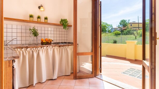 Uma cozinha com painel de azulejos, bancada e porta que dá para uma varanda.
