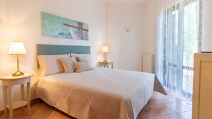 Quarto com cama grande, duas mesas de cabeceira com abajures, um quadro na parede e uma janela com cortinas.