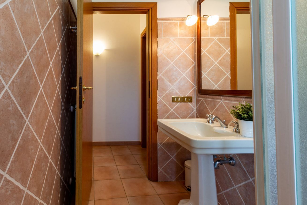 Un bagno con un lavandino bianco, uno specchio e una porta che dà su un'altra stanza.