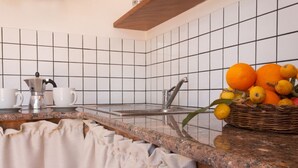 Cozinha com bancada de granito, cafeteira, pia e cesta de laranjas e limões.