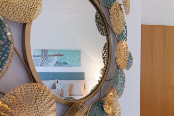 A bedroom with a bed, a wall-mounted mirror, and a painting of a beach scene.