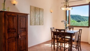 Uma área de jantar com mesa e cadeiras de madeira, um painel decorativo na parede e uma janela com vista para o verde.