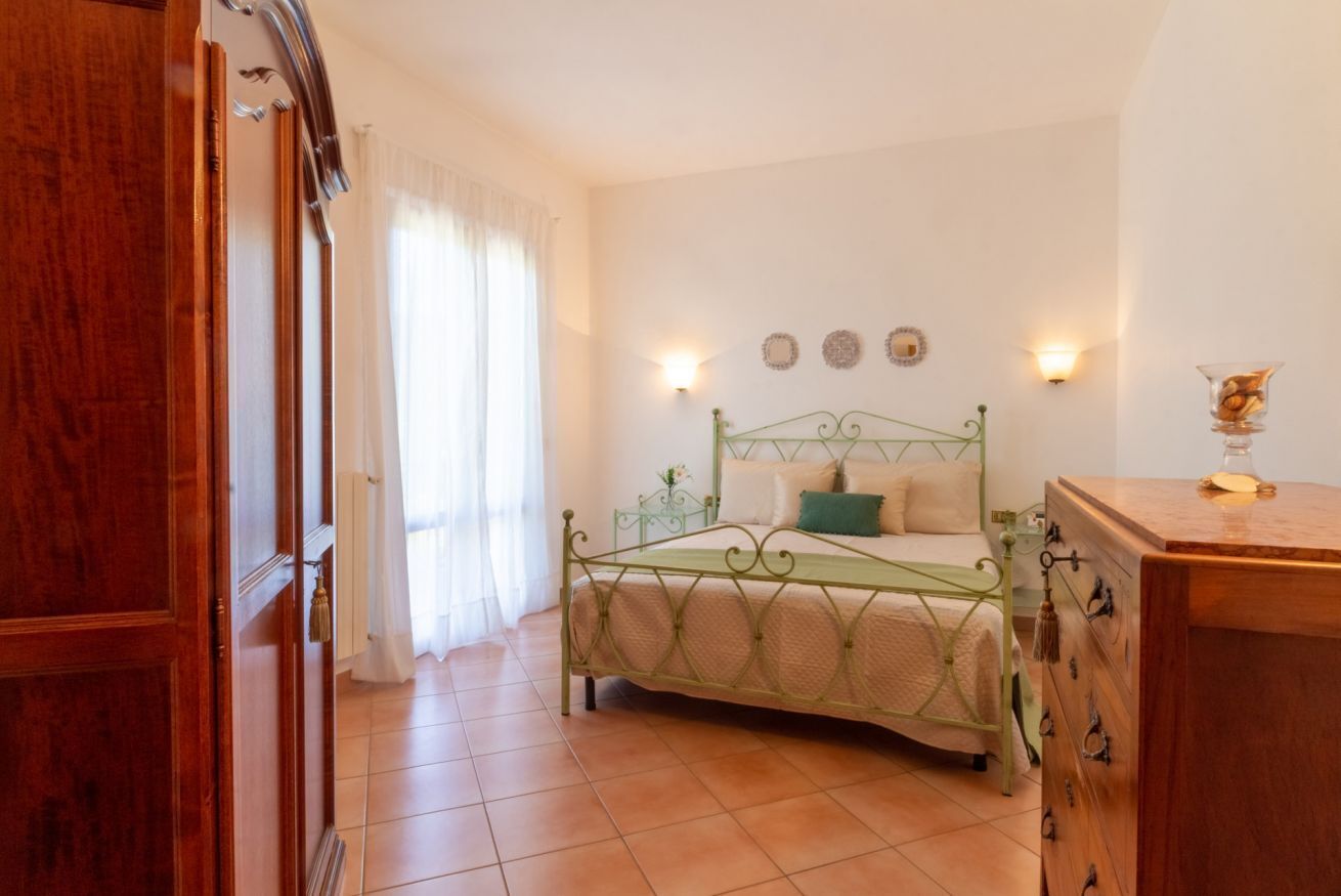 Quarto com cama, penteadeira, janela com cortinas e arandelas na parede.