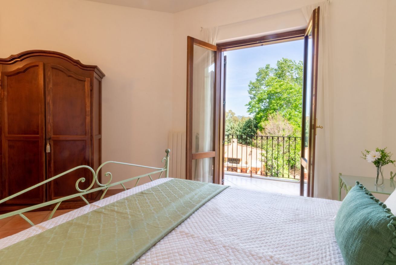 Ein Schlafzimmer mit Bett, Kleiderschrank und einem Balkon mit Blick auf Grünflächen.