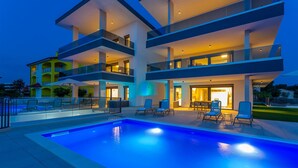 Un immeuble moderne à plusieurs étages, doté d’une piscine et d’un espace extérieur aménagé pour se détendre.