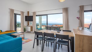 Un salon moderne comprenant un canapé, une table à manger, des chaises, un téléviseur et une vue sur la mer.