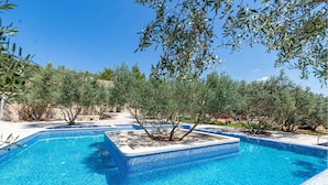 A clear blue pool surrounded by olive trees and a stone wall.