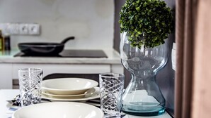 Una mesa de comedor dispuesta con platos blancos, cristalería transparente y cubiertos. Un florero de vidrio decorativo con una planta verde está sobre la mesa.