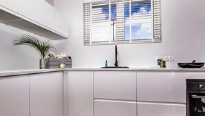 Una cocina moderna con armarios blancos, un grifo negro y una ventana con persianas.