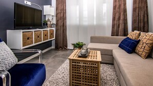 Una sala de estar moderna con un televisor de pantalla plana, un sofá con cojines estampados, una mesita de madera y una planta decorativa.